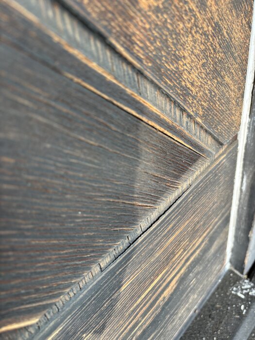 Närbild på trädetalj på en ytterdörr med sprickor och flagor; ytan är sandpapprad och skadad, träet ser torrt och slitet ut.