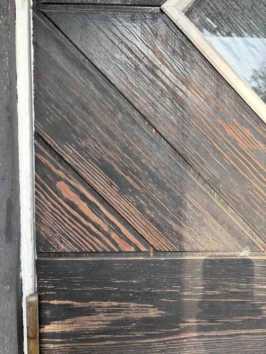 Närbild på en ytterdörr med mörkt trä, lacken har flagnat och träet ser torrt ut. Vissa delar av träet verkar vara på väg att lossna.