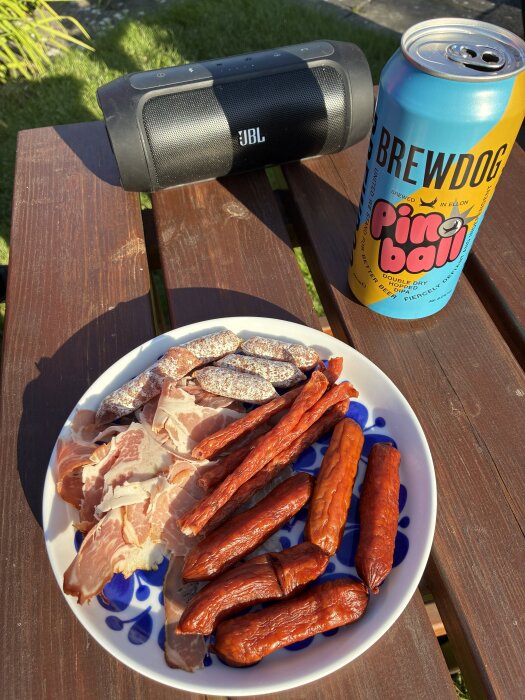 Tallrik med charkuterier och Brewdog öl vid en högtalare på ett trädäck i solen.