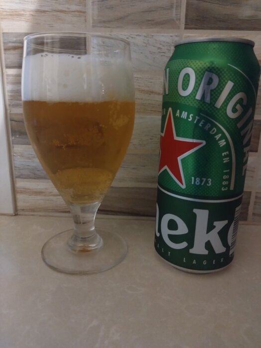 Ett glas fyllt med öl bredvid en grön burk märkt med Heinekens logotyp och text.