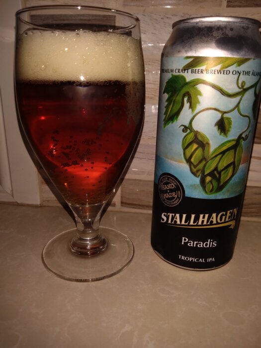 Ett glas med skummande öl och en burk Stallhagen Paradis Tropical IPA på ett bord.
