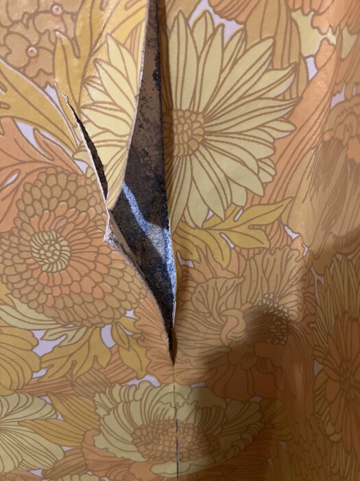 Ripped floral wallpaper revealing damaged wall beneath.