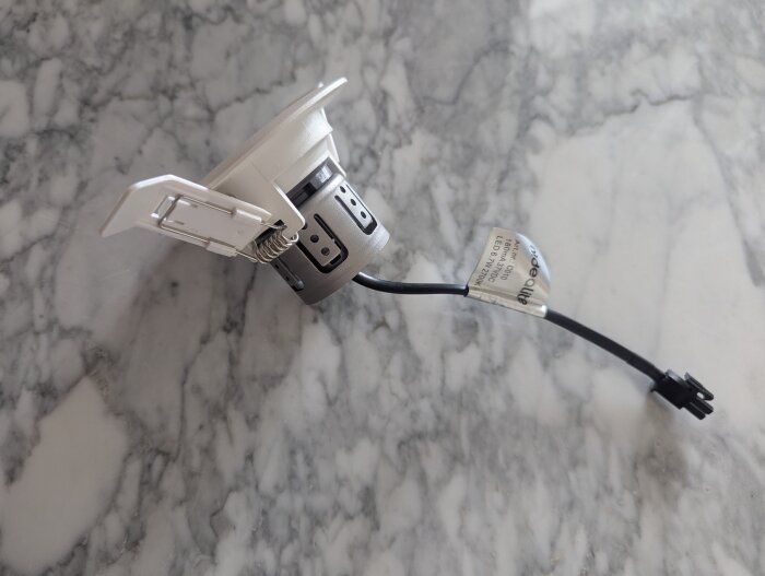 Spotlight med svart kabel och vit hölje placerad på en marmoryta. Lampan är av en äldre modell som inte längre tillverkas.