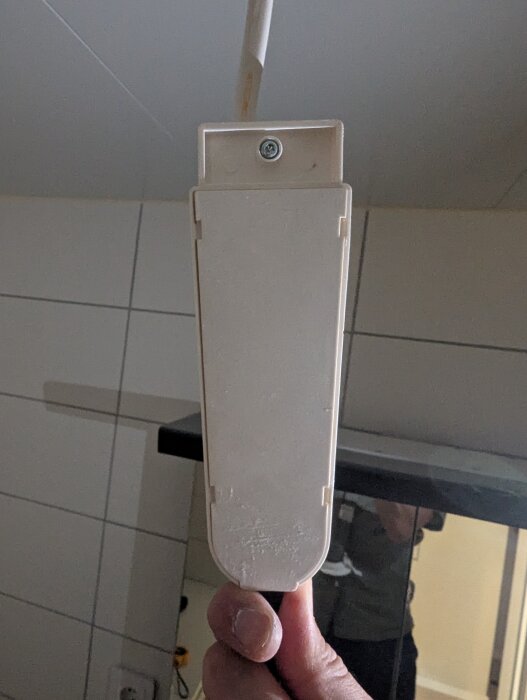 Närbild på en spotlight-armatur från badrummet, hållen i handen, med sladd och skruv synliga.