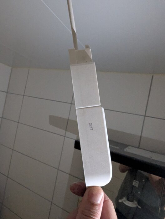 Vit spotlight med nummer "2217" hålls upp mot ett kaklat badrumstak, kopplad med två kablar.