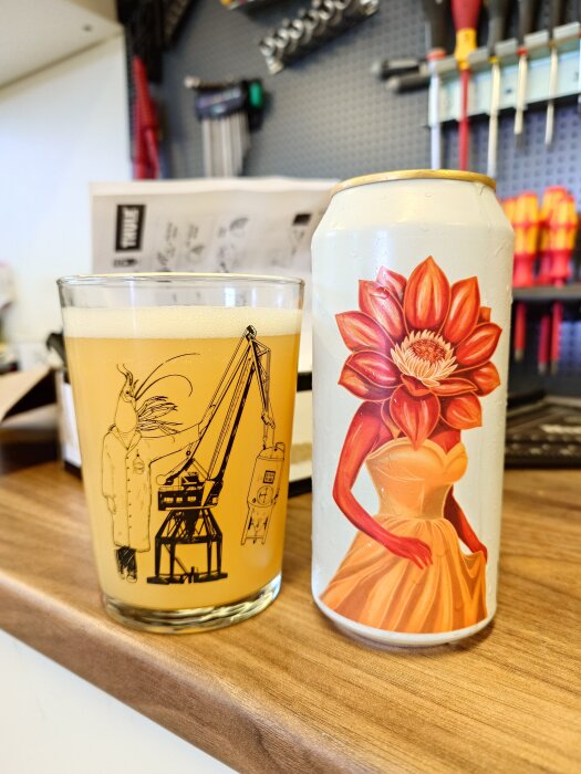 Öl i glas och burk på träyta, burken har konstverk av person med blomma som huvud. Verktyg i bakgrunden.