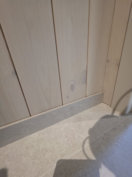 Träpanel med klinkerkant vid golvet i en attefallstoalett. Golvet är klinkrat och en klinkerlist är monterad mot väggen.