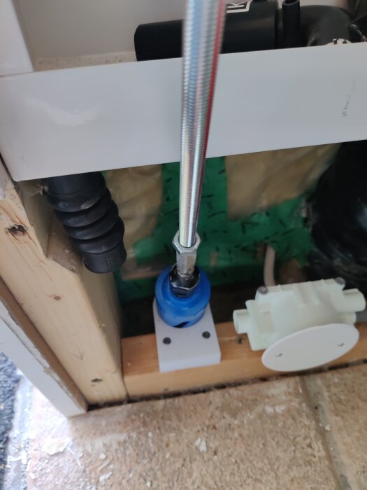 Bilden visar ett rörsystem med en koppling i blått fästat vid ett träramverk. En metalledning med ett skyddande hölje är ansluten ovanpå.