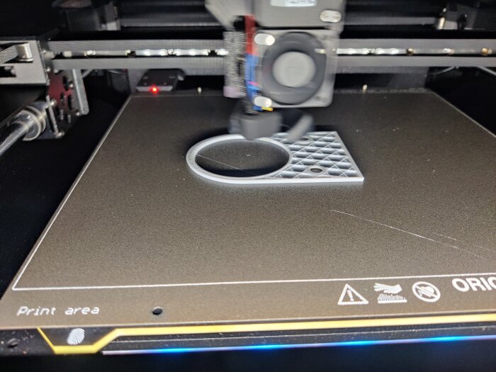 3D-skrivare i arbete med att skapa en adapter för hålsåg, på bild syns tryckplattan med halvfärdigt 3D-tryck i plast.