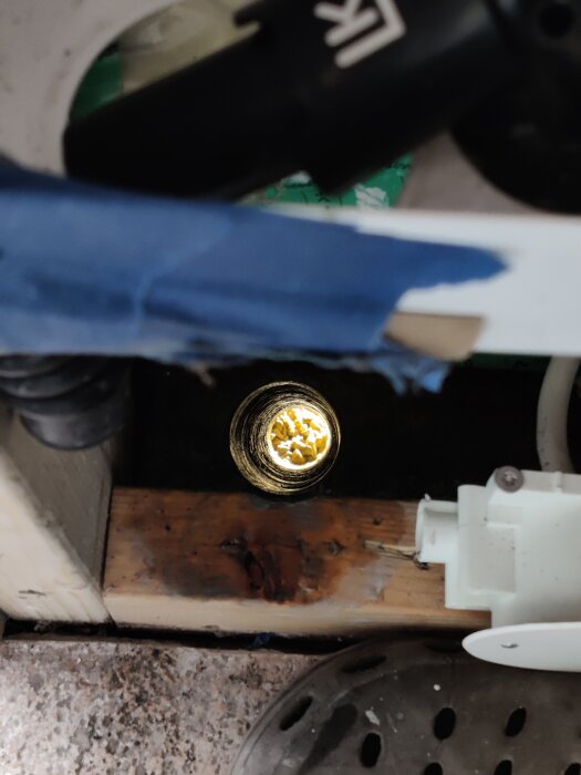 Synligt nyborrat hål genom plankgolv, omgivet av verktyg och skyddsrör, i ett projekt för att installera PEM-slang genom ett skyddsrör.