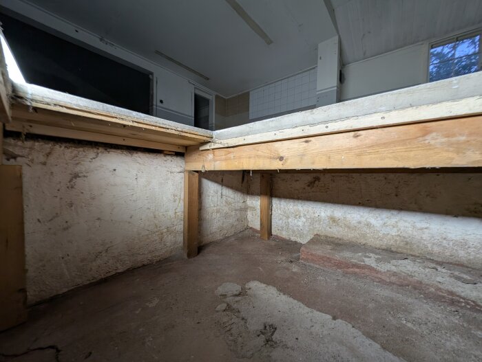 Underifrånvy av garagegolv med träreglar över betonggolv, reglarna stöder en upphöjd golvplatta. Viss slitage och smuts syns på betongen.