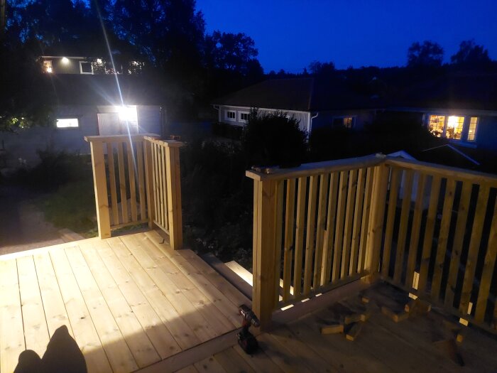 Nattbild av nyligen byggd trätrappa med räcken och spotlights installerade i stegen, omgivna av mörka skuggor och träd i bakgrunden.