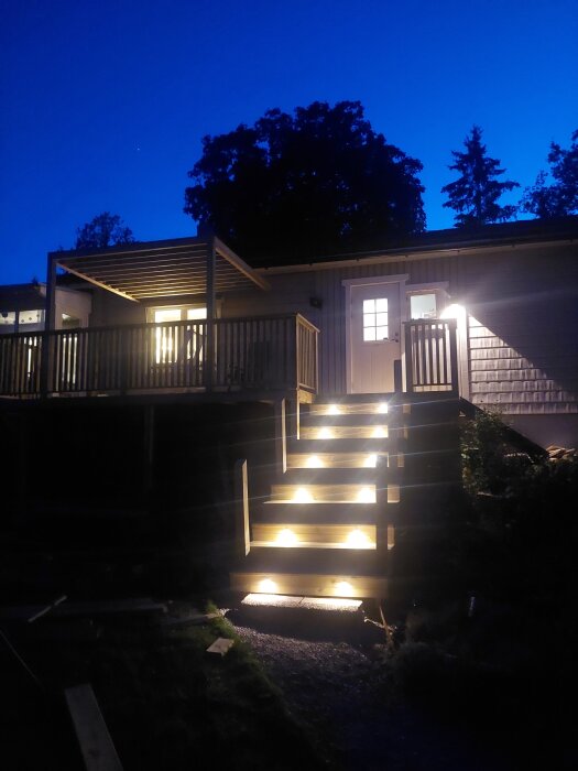 Utomhustrappa med inbyggda spottar på vartannat steg, mot en veranda under kvällshimmel.