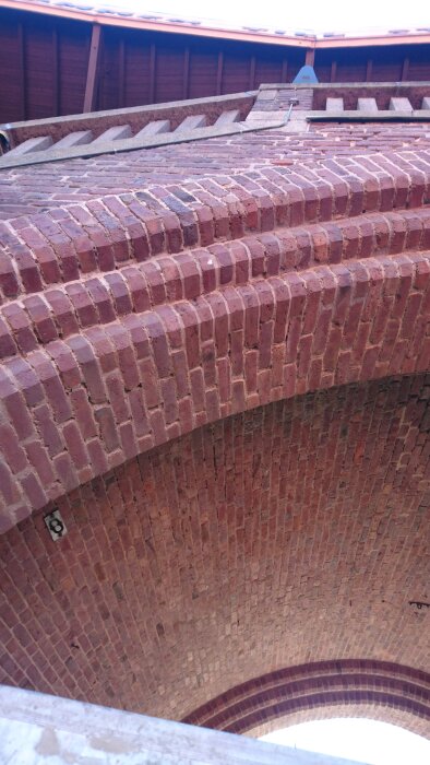 Bågformad tegelfasad på Stockholm Stadion med varierande färgtoner från puts och kalkfärg, visar hantverkets utmaningar.