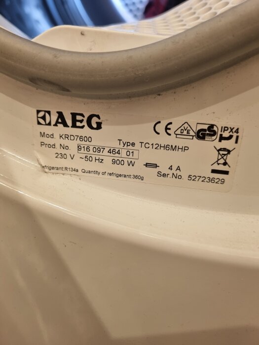 Etikett på AEG-torktumlare med modellnummer KRD7600 och serienummer 52723629, visar specifikationer som 900 W, 230 V och kylmedel R134a.