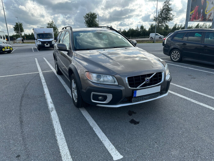 Grå Volvo parkerad på en parkeringsplats en molnig dag, bilen står inte rakt i rutan.
