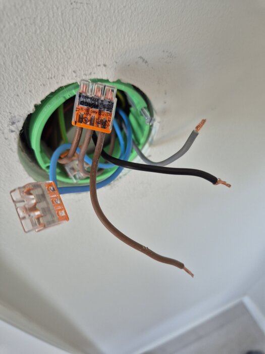 Elektriska kablar och kopplingsblock i en väggöppning, visar kopplad och okopplad ledning i samband med spotlightlampa som lyser konstant.