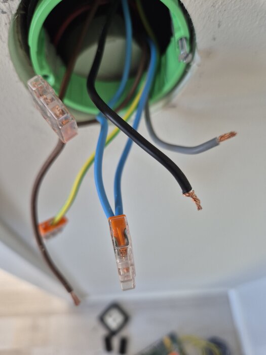 Lös trådkoppling med synliga koppartrådar i lamputtag; gröna, gula, blå kablar delvis kopplade, andra lösa.