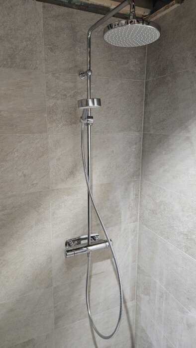 Dusch med kromblandare och regnduschhuvud monterad i ett kaklat badrumshörn.