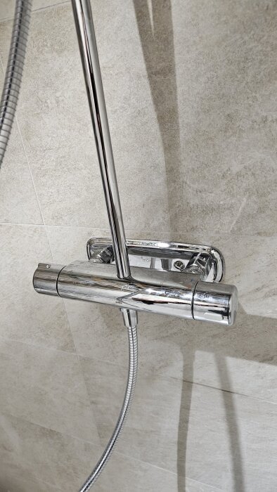 Kromad duschblandare monterad på vägg, visar vred för temperaturjustering och duschslang.