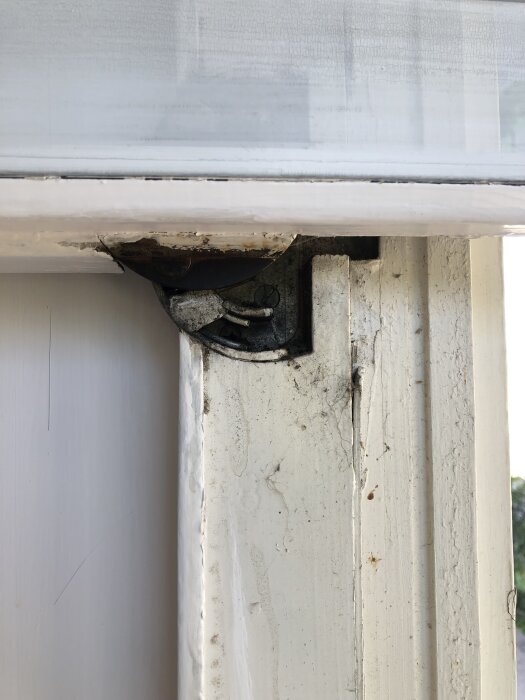 Gångjärn på 50-talsfönster med synlig spärrmekanism och smuts, nära träkarmen.