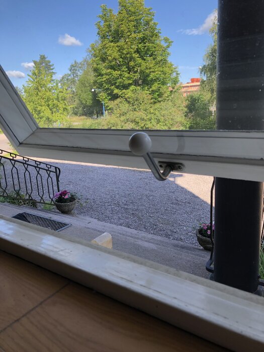 50-talsfönster öppet utåt med vy över en trädgård, gångjärn synligt nära en spärr på fönsterkarmen.