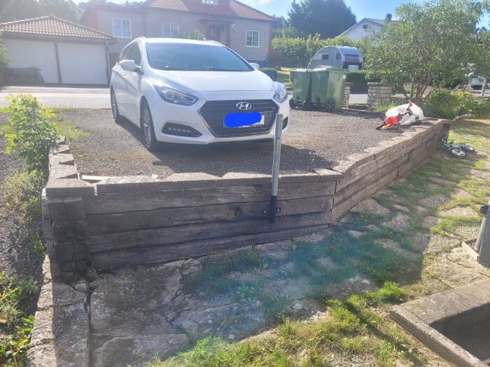 En parkering med en vit bil ovanpå en upphöjd yta omgiven av gamla, delvis ruttna slipers.