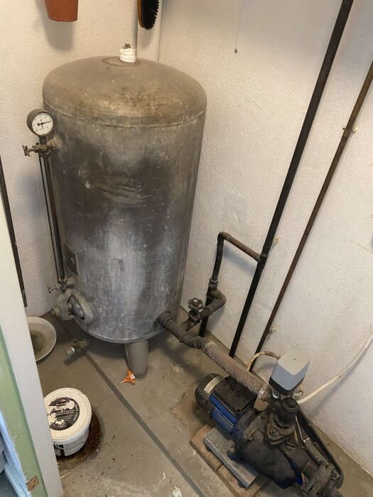 Gammal TMV elpanna från 70-talet med rör och en tryckmätare, placerad i ett hörn av ett rum med några tillhörande komponenter på golvet.