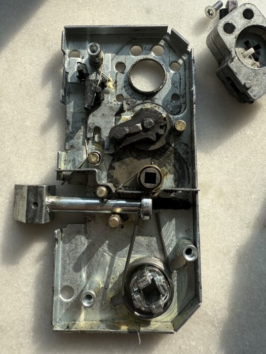 Metalldel av ett dörrlås på en yta med skruv bredvid, visar mekaniska komponenter och möjliga slitage.