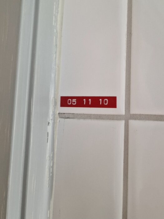 Rött etikett på vit kakelvägg med texten "05 11 10".