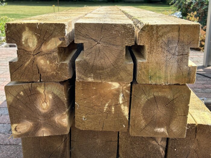 Staplade trästolpar med urtag på en gård, omgivna av gräs och buskar.