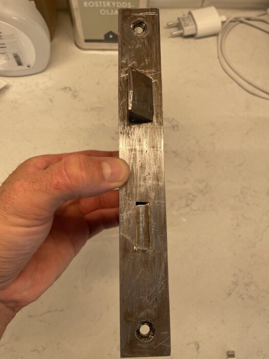 Gammal metallisk låskista som hålls i hand, del av dörrrenovering. Ytan är repig och har kvarvarande smuts trots rengöringsförsök.