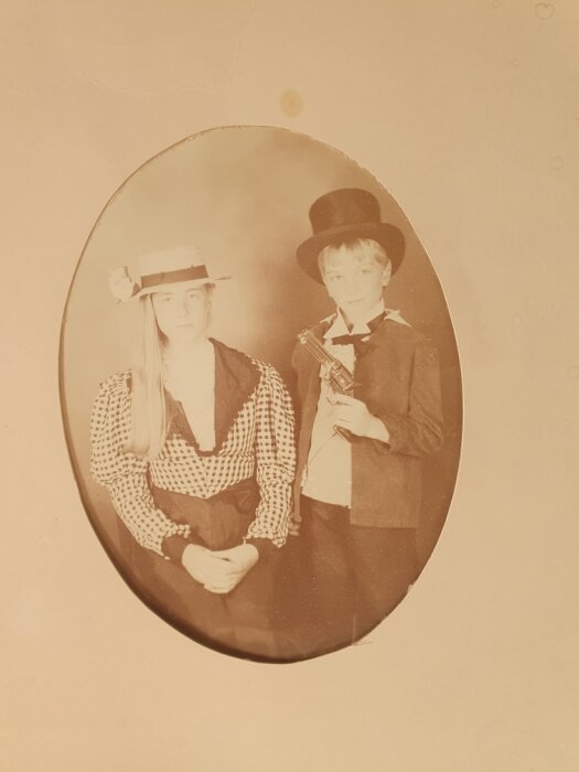 Två personer klädda i gammaldags kläder; kvinna med hatt och man med hög hatt och leksakspistol, vintage-stil foto från High Chaparral.