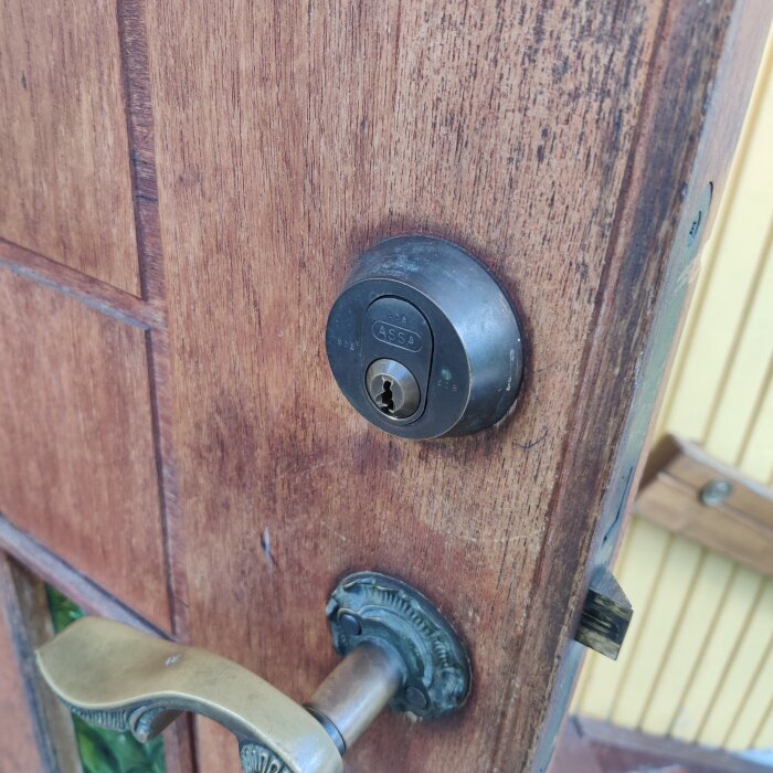 Brunt trä dörr med ett ASSA-lås och mässingshandtag, fokus på låscylindern.