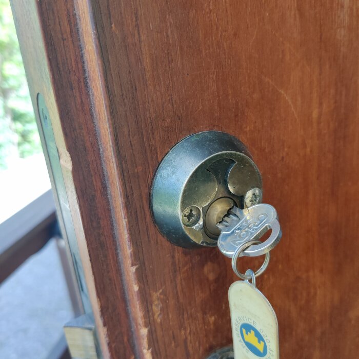 Närbild av ett lås på en entrédörr i trä med en nyckel insatt. Nyckeln har en nyckelring med en gul etikett.