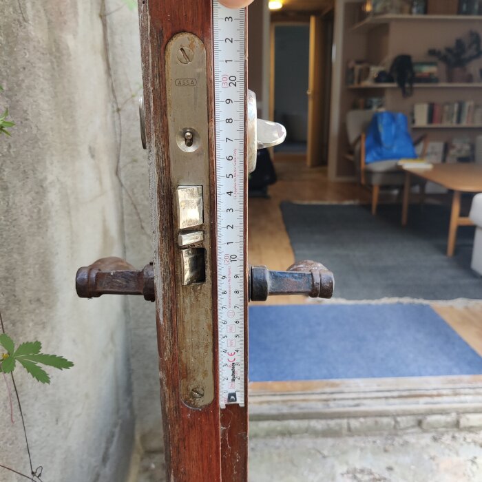 Närbild på en dörrkarm med ett lås märkt "ASSA" och en linjal som mäter dörrens låshus. Inre del av bostaden syns i bakgrunden.