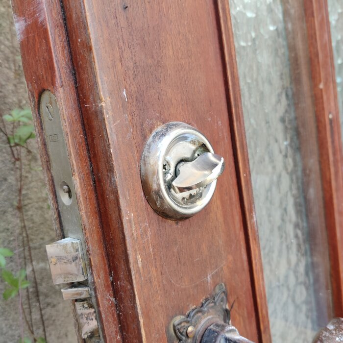 Äldre trädörr med metallvred och lås synliga, delvis öppet låshus.