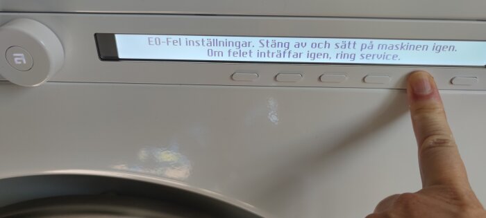 Finger pekar på display med felmeddelande "E0-Fel inställningar. Stäng av och sätt på maskinen igen. Om felet inträffar igen, ring service.