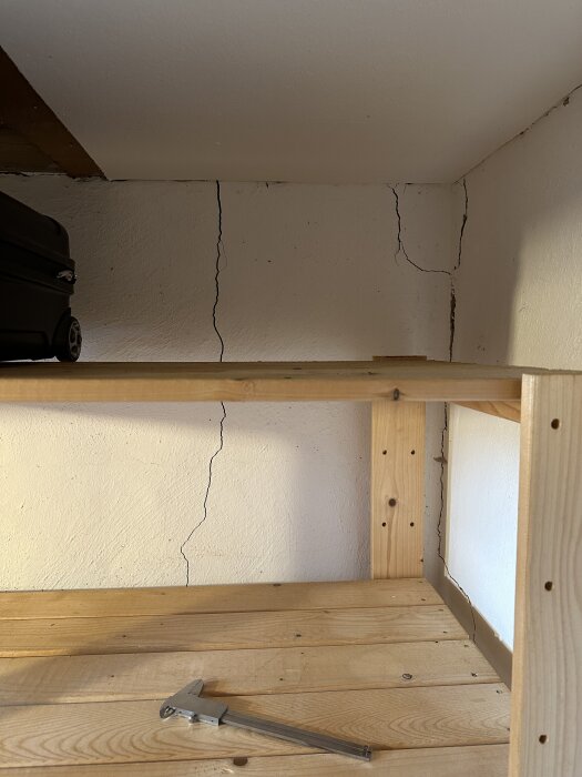 Spricka i källarvägg synlig bakom hylla, ljus tränger igenom. En tumstock ligger på hyllan.