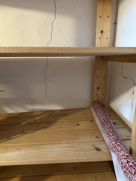 Spricka i källarvägg bakom trähylla, visar dagsljus genom sprickan i gammalt hus.