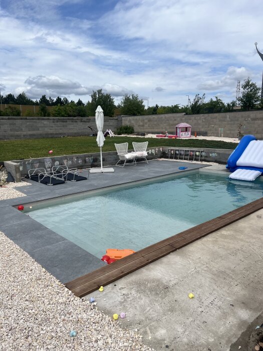 Utomhuspool med halvfärdig terrass och leksaker; grön gräsmatta och rosa lekstuga i bakgrunden.