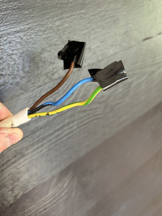 Färgglada elektriska kablar (brun, blå, gul/grön) med svarta anslutningar visas mot en grå bakgrund.