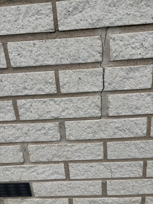 Murverk av vita tegelstenar med synlig spricka mellan två stenar.