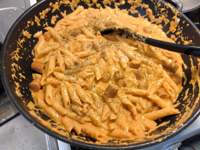 Krämig pasta i krämig sås med grillad paprika och kabanoss i en stekpanna, toppad med kryddor.