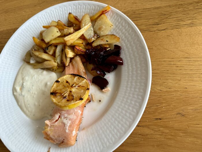 Grillad lax på citronskivor, serverad med fetaostsås och ugnsbakade rotfrukter på en vit tallrik.