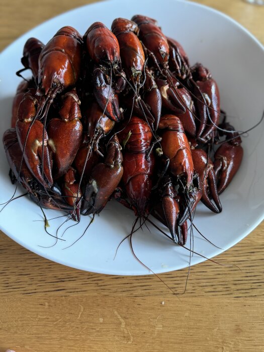 En tallrik med kokta kräftor, rödbruna till färgen, upplagda på ett ljus träbord.