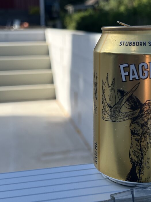 Början av en ölburk med ett hjortmotiv syns i förgrunden, trappa och byggarbetsplats suddig i bakgrunden.