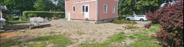 Torftig gräsmatta framför ett rosa hus efter dränering, med kvarvarande återfyllnadsmaterial och sparsam vegetation.