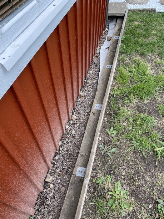 Nymålad röd vägg med smutsstänk, kant med stenar och gräs vid marken, diskussion om orsaken till smutsstänk på väggen.