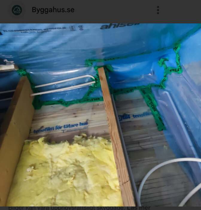 Blå diffusionsspärr tejpad med grön tejp över isolering och träpanel, del av byggprojekt.